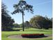 Scenic golf course view with a well-maintained green, decorative flower bed and mature trees set against a clear blue sky at 5224 88Th E St, Bradenton, FL 34211
