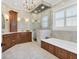 Luxurious primary bathroom featuring wood cabinets, a soaking tub, an elegant chandelier, and frameless glass shower at 6600 Horned Owl Pl, Sarasota, FL 34241