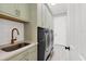 Bright laundry room with modern washer/dryer units, white subway tile backsplash, and light green cabinets at 6600 Horned Owl Pl, Sarasota, FL 34241