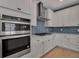 Close-up of the well-equipped kitchen featuring stainless steel oven, cooktop, hood, and stylish blue backsplash at 8726 Backshore Ln, Parrish, FL 34219