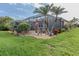 Back of home with screened in patio, tropical foliage, and a well maintained lawn at 2160 Chenille Ct, Venice, FL 34292