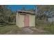 View of a weathered shed with peeling yellow paint and pink door sitting in an overgrown lot at 2230 Myakka Rd, Sarasota, FL 34240
