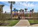 Community playground featuring modern play structures, swings, and mature palm trees against a backdrop of blue skies at 5311 White Sand Cv, Bradenton, FL 34211