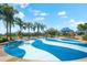 A splash pad area with blue and white wavy patterns, surrounded by palm trees and playground equipment, perfect for summer fun at 4954 Newport News Cir, Lakewood Ranch, FL 34211