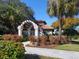 Charming clubhouse entrance featuring a tiled roof, stone archway, and beautifully landscaped surroundings at 5087 Timber Chase Way, Sarasota, FL 34238