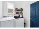 Neat laundry room with modern washer and dryer, floating shelves, and a blue painted door at 5806 43Rd E Ct, Bradenton, FL 34203