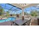 Covered and screened patio area featuring a dining table, grill, and scenic views of the pool and backyard at 7340 Barclay Ct, University Park, FL 34201