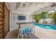 Outdoor bar area with a large TV for entertainment, views of the pool, and a tropical landscaped yard at 785 Jacaranda Rd, Anna Maria, FL 34216