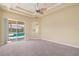 Carpeted primary bedroom offering a tray ceiling, ceiling fan, and access to the pool and patio area at 5270 White Ibis Dr, North Port, FL 34287