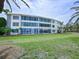 A multi-story condo building with walls of windows, framed by a green lawn and lush tropical landscaping at 100 Sands Point Rd # 225, Longboat Key, FL 34228