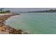 A scenic waterfront view featuring rocky shoreline and clear turquoise water with bridge and houses in the background at 100 Sands Point Rd # 225, Longboat Key, FL 34228
