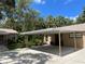 Single-story home featuring a covered parking area surrounded by mature trees and greenery at 5013 Village Gardens Dr # 34, Sarasota, FL 34234