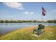 Scenic view of a serene lake with a bench and American flag, providing a peaceful retreat at 11790 Fennemore Way, Parrish, FL 34219