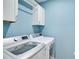 Bright laundry room with washer, dryer, and white storage cabinets against blue wall at 15408 Trinity Fall Way, Bradenton, FL 34212
