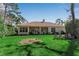 Back exterior showcasing a covered patio, lush lawn, mature trees, and seating area overlooking the lake at 402 Walls Way, Osprey, FL 34229