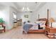 Bright main bedroom features a four-poster bed, light hardwood floors, and a tray ceiling with modern chandelier at 402 Walls Way, Osprey, FL 34229