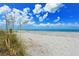 Expansive white sand beach with scattered vegetation under a blue sky filled with puffy clouds at 8779 Midnight Pass Rd # 106H, Sarasota, FL 34242