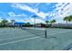 Outdoor tennis court with net, surrounded by palm trees, with a covered seating area and blue skies in the background at 5562 Rain Lily Ct, Sarasota, FL 34238