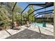 Screened-in pool area with two lounge chairs on the brick patio and lush green surroundings at 12352 Auburndale Ct, Venice, FL 34293