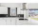Modern kitchen featuring a sleek black backsplash, white cabinets, and stainless steel range hood at 203 22Nd Ne St, Bradenton, FL 34208