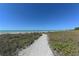 Scenic beach path leading to the ocean with beautiful blue sky and lush vegetation on either side at 8735 Midnight Pass Rd # 301B, Sarasota, FL 34242