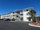 Bright white condo building with outdoor stairs, parking, and landscaping under a clear blue sky at 1633 Leisure Dr # M-37, Bradenton, FL 34207