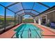 Enclosed pool area featuring an in-ground pool, red flooring, and seating area with chairs and sliding glass doors to the home's interior at 457 Lake Of The Woods Dr, Venice, FL 34293