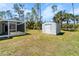 Backyard featuring a screened-in patio and a storage shed surrounded by lush grass and mature trees at 3865 N Cranberry Blvd, North Port, FL 34286