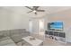 Comfortable living room featuring a plush sofa, ceiling fan, and decorative shelving unit with a large television at 8918 Waxwing Way, Parrish, FL 34219
