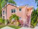 Bright pink two-story home featuring white accents, tropical landscaping, and a stairwell leading to the front door at 5500 Longwood Run Blvd # 201, Sarasota, FL 34243