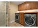 Laundry room with a glass shower and modern washer and dryer units and wood cabinets above, offering convenience and storage at 5512 Avenida Del Mare, Sarasota, FL 34242
