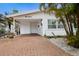 A well-kept exterior of the home shows a brick driveway and carport with a white facade and manicured tropical plants at 415 63Rd St, Holmes Beach, FL 34217