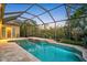 Screened pool with rock waterfall feature surrounded by lush landscaping at sunset at 13 Bayhead Ln, Osprey, FL 34229