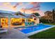 Backyard oasis featuring a sparkling pool, comfortable seating, an outdoor kitchen, and lush tropical landscaping at twilight at 527 Key Royale Dr, Holmes Beach, FL 34217
