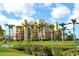 Exterior shot of the grand building surrounded by lush greenery and palm trees with a water view at 611 Riviera Dunes Way # 107, Palmetto, FL 34221