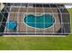 A screened-in pool features a unique shape, surrounded by a textured patio and a blue umbrella with chairs at 3606 Garden Lakes Clenet, Bradenton, FL 34203