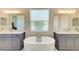Modern bathroom featuring dual sinks, sleek gray cabinets, and a luxurious soaking tub beneath a bright window at 14277 Skipping Stone Loop, Parrish, FL 34219