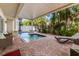 Inviting covered pool area with lush tropical landscaping, lounge chairs, and brick paved patio at 2309 Avenue C # 100, Bradenton Beach, FL 34217