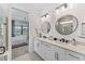 Bright bathroom featuring double vanity with white cabinets, round mirrors, and a view to the main bedroom at 6260 Fish Eagle Ct, Nokomis, FL 34275