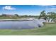 Scenic golf course view featuring a tranquil pond, lush green grass, sand traps, and a distant clubhouse with a red roof at 7309 Regina Royale Blvd # 21, Sarasota, FL 34238