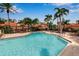 A lovely outdoor pool area surrounded by tropical landscaping, lounge chairs, and red umbrellas at 7309 Regina Royale Blvd # 21, Sarasota, FL 34238