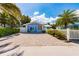Charming blue bungalow featuring a brick driveway, white picket fence, and tropical landscaping at 113 Palm Ave, Anna Maria, FL 34216