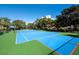 Brightly painted tennis court with green and blue surface surrounded by lush trees on a sunny day at 1928 Harbourside Dr # 1404, Longboat Key, FL 34228