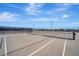 A rooftop tennis court featuring a gray surface, white lines, black net and fencing under a blue sky with some clouds at 808 3Rd W Ave # 214, Bradenton, FL 34205