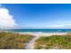 A pristine sandy beach meets the turquoise ocean under a clear blue sky, framed by native dune grasses at 845 Benjamin Franklin Dr # 104, Sarasota, FL 34236