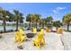 Outdoor fire pit area with yellow Adirondack chairs surrounded by palm trees and a lake view at 9215 Royal River Cir, Parrish, FL 34219