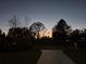 Home exterior at sunset with driveway, lawn, and mature trees silhouetted against the colorful sky at 1750 Gold Ave, Sarasota, FL 34235