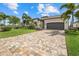 Charming single-story home featuring a brick paver driveway, a gray two-car garage, and lush landscaping with palm trees at 5811 Brandon Run, Bradenton, FL 34211