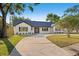 Charming one-story home boasts a white brick facade, black trim, and a spacious circular driveway at 1406 N Riverhills Dr, Temple Terrace, FL 33617