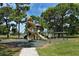 Community playground featuring a play structure with a slide set amongst trees at 568 Sheridan Dr, Venice, FL 34293